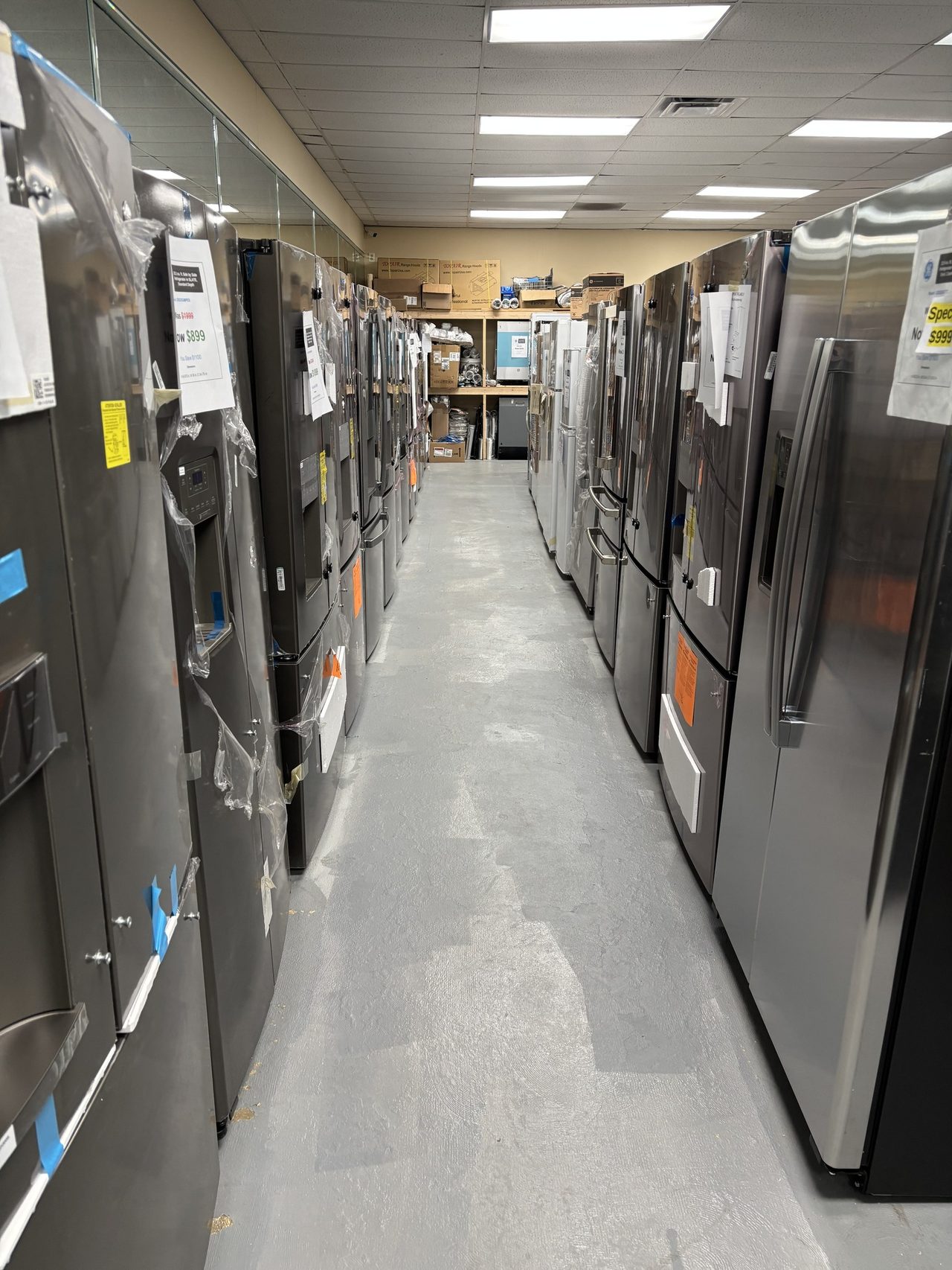 Long aisle of stainless side-by-side and french-door refrigerators in the Canal St wholesale warehouse